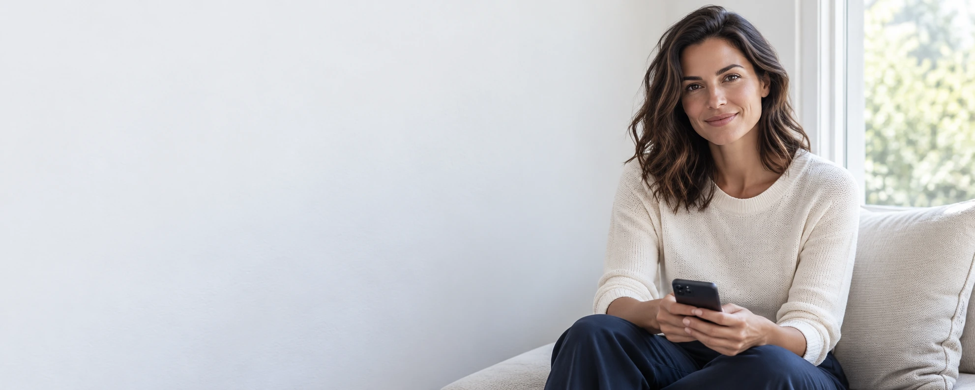 A woman by a bright window checking her phone for the deposit